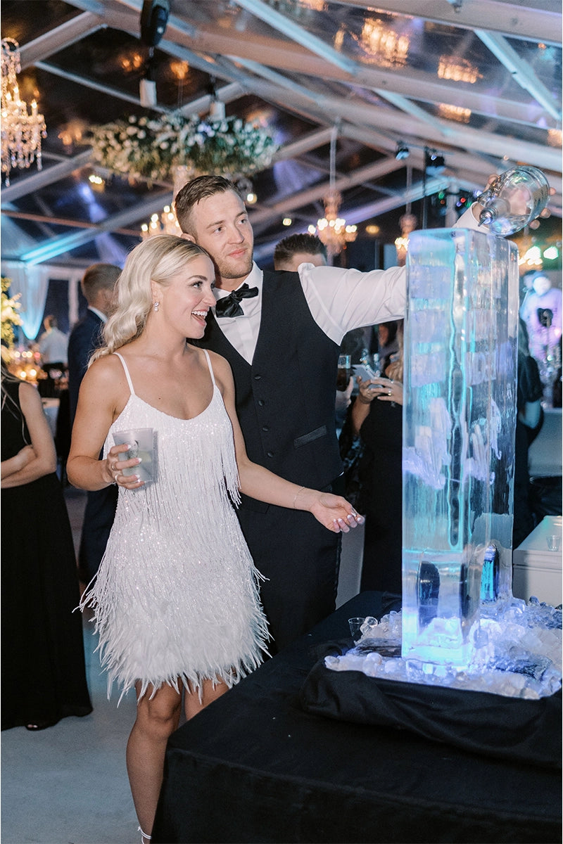 happy bride and groom enjoying ice sculpture luge